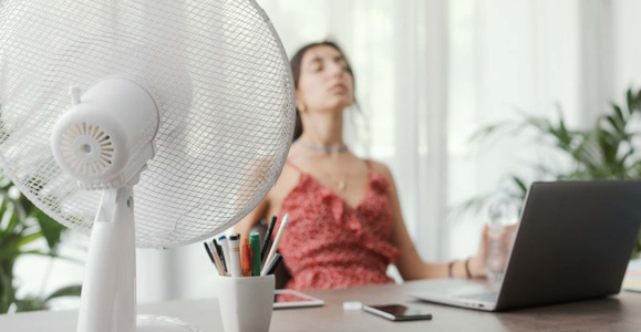 Woman sitting at a desk with a ventilator in front of her, illustrating a heatwave