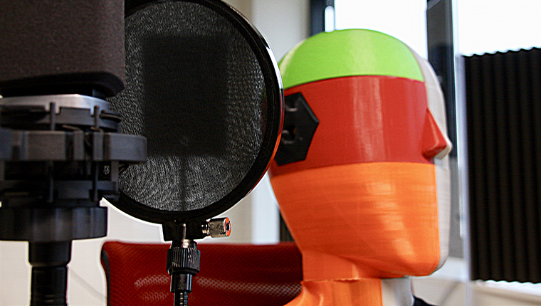 Close-up of professional microphone with 3D printed, colourful listening dummy behind